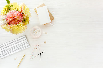 Flat lay women's office desk. Female workspace with pink and yellow dahlias and roses flowers bouquet, accessories, golden diary, glasses on white wooden 