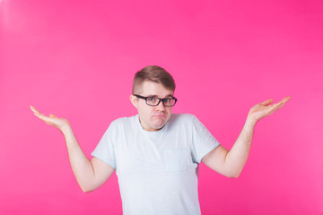 Portrait of confused man showing I don't know gesture on pink background