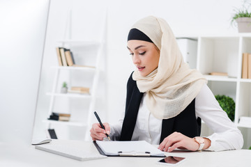 portrait of focused muslim businesswoman signing papers at workplace