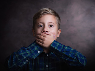 Portrait of cute little boy closed mouth with his hand, studio shot