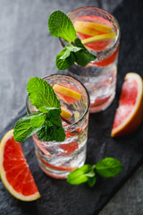 Cold beverages with grapefruit and mint on black serving board.