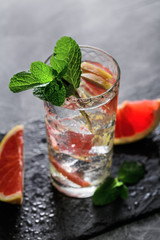 Cold cocktail with grapefruit and mint on black serving board.