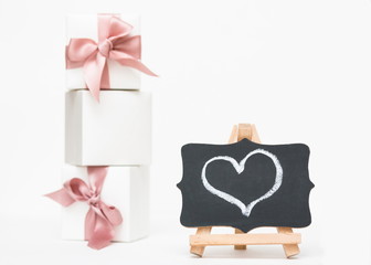 White gift boxes of the famous jewelry brand with charms bracelets with a pink ribbon. A bottle of perfume and little hearts. Mock up. Empty place for an inscription. Postcard for the holiday. 