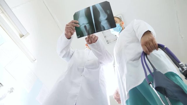 Male medics consult with each other while looking at x ray image. Two caucasian doctors view mri picture and discussing about it. Medical workers in hospital examine x-ray prints. Low angle of view
