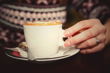 Closeup of female hand is holding a cup of coffee on wooden table