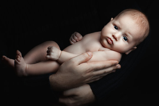 Portrait of a cute baby girl in the dark. Men's hands hold the child