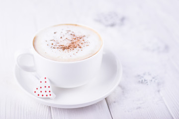 Happy Valentine's day! White cup with cappuccino and red heart on a white wooden background. Free space
