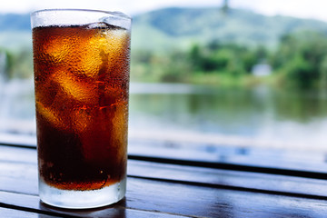Cola in glass on table with mountain and river background