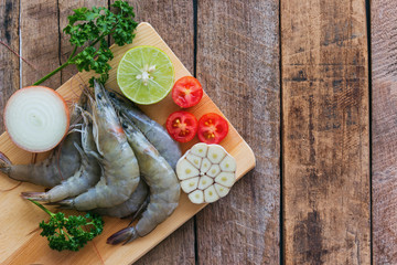 Fresh white shrimps on wood cutting board in top view flat lay with copy space. Prepared raw prawn and vegetable and herbs for cooking seafood menu on wooden table. Homemade delicious food concept.