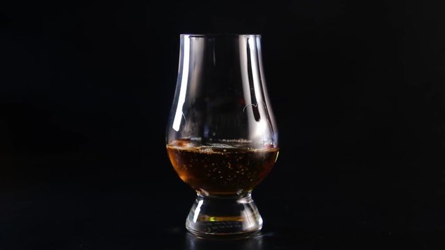 Bartender's hand pouring alcohol into glass on black background.