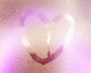 Pink color blurred lovely heart symbol drawn by hand on the wet rainy glass. Valentines day.