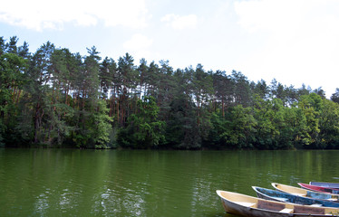 View of beautiful clean lake in forest among trees and boats on water. Romantic atmosphere in peaceful place outdoors, summer rest on nature.