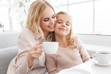 mother and daughter cuddling while drinking tea in cafe
