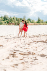 Happy pregnant woman and her husband walk together on the sand.