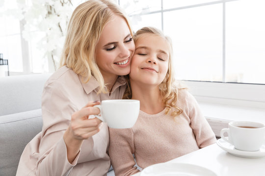 mother and daughter cuddling while drinking tea in cafe