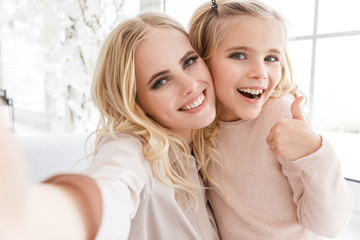 young beautiful mother and daughter taking selfie and showing thumb up