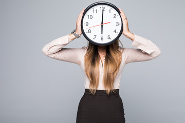 Business woman holding a clock in front of her head against a grey background