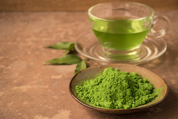Close up of green tea powder with glass cup of hot tea on the table. Free space for text