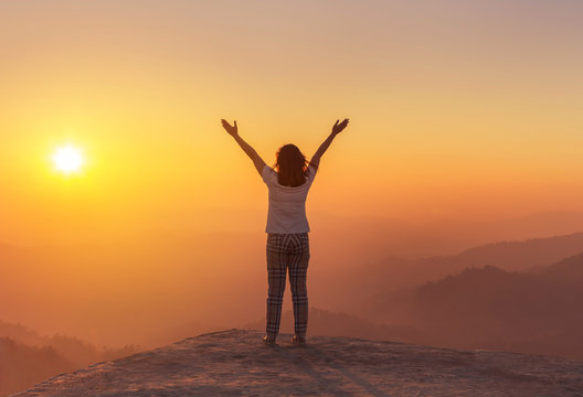             Silhouette Back Of Woman Stand Raising Up Two Arm Embrac Enjoying To Valley View On High Cliff Over Rainforest Mountains To Sunlight In Sunset    