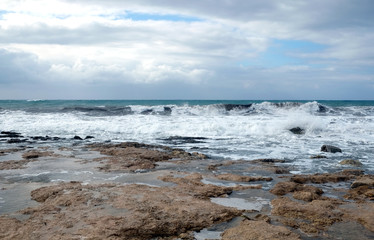 Fototapeta na wymiar Storm waves break about the coastal stones against the cloudy sky on overcast day
