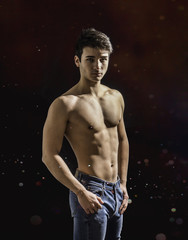 Fototapeta na wymiar Handsome, fit muscular young man shirtless, wearing only jeans standing on black background, looking at camera