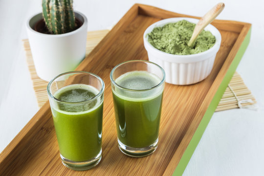 Two wheatgrass shots with powdered wheatgrass and wooden spoon