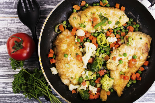 fried chicken fillet with spices in a frying pan and vegetables