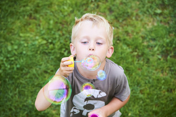 Young boy blowing bubbles with green grass lawn background
