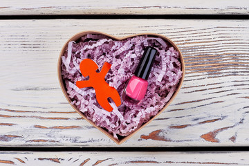 Gift for a young girl. Pink nail polish and red figurine in heart-shaped box with soft padding. Celebrating birthday or Valentine's day.