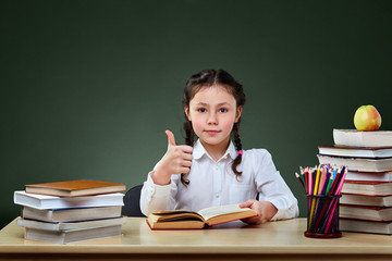 Girl with books points on green chalkboard