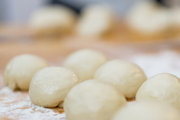 Fototapeta na wymiar Closeup of ball ready dough on floured kitchen table. Defokus in the background.