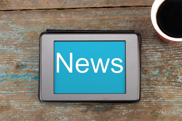 News -  inscription on tablet screen. Tablet  and cup of coffee on the wooden background