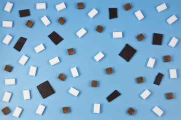 Fototapeta na wymiar Sweets pattern. Brown and white sugar cubes and chocolate pieces on blue background.