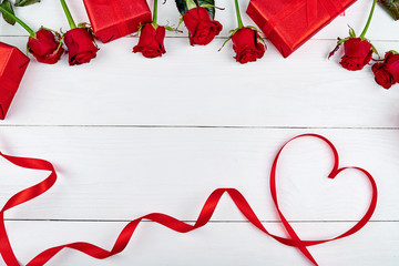 Top view of red roses, gift boxes and ribbon shaped as heart on white wooden background, copy space. Greeting card mockup for Valentines Day, Womans Day, flat lay. Love concept