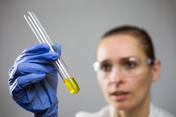 young woman in the lab, hand in a blue glove holds a test tube with yellow liquid, goggles, white robe. concept of research in the field of medicine. close up, selective focus , blurred background