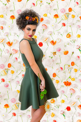 Brown hair attractive woman in a green dress with colorful daisies in hair on flower wall. Spring concept