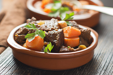 Beef meat stewed with carrots and spices in ceramic pot  on old black wooden board. Selective focus.
