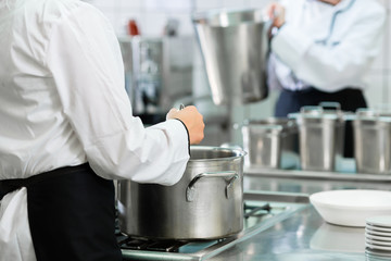 Chefs at stove in professional catering kitchen stirring in pots