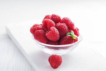 Fresh raspberries in glass bowl on white wooden board, with copy space. Selective focus.
