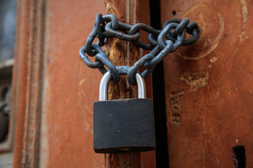 Wooden brown peeled door for background. Padlock with chain forbidden the entrance. Close up, detail