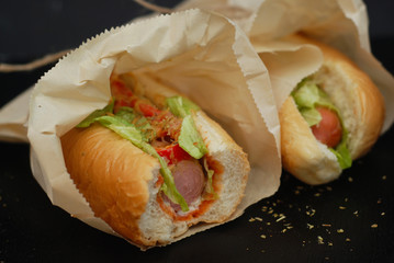 Fast Food. Close up Hotdogs with Letuce, Tomatoes And Ketchup. Black Table with Spices. Healthy Homemade Food.