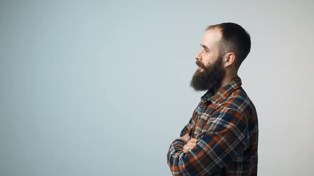 Closeup profile of confident hipster bearded man standing with folded hands looking forward isolated on gray background, turning to camera and gesturing thumb up