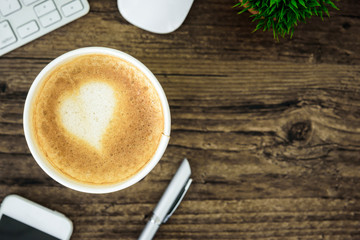 A latte coffee with art heart milk on the brown wood desk table from top view and copy space. Flat lay with desk, business and valentine concept.