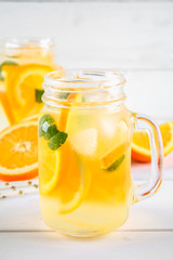 Orange detox water in mason jars on a white wooden table. Healthy food, drinks.