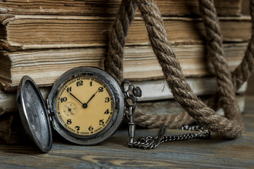 Old books with pocket clock on a wooden table