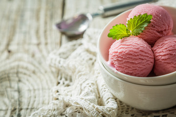 Raspberry ice cream in white bowl, rustic wood background