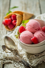 Raspberry ice cream in white bowl, rustic wood background