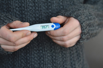 Man hands holding digital thermometer with high temperature in warm knitted sweater