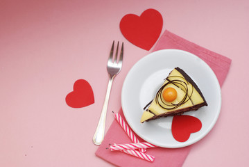 Valentine's Day. Slice of Chocolate Cake with Red Paper Hearts and Fork with Pink Napkin on Pink Background.