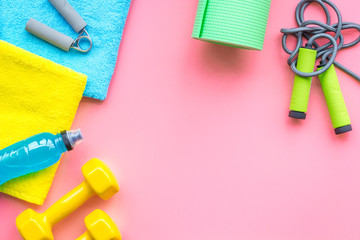 Fitness background. Equipment for gym and home. Jump rope, dumbbells, expander, mat, water on pastel pink background top view copy space
